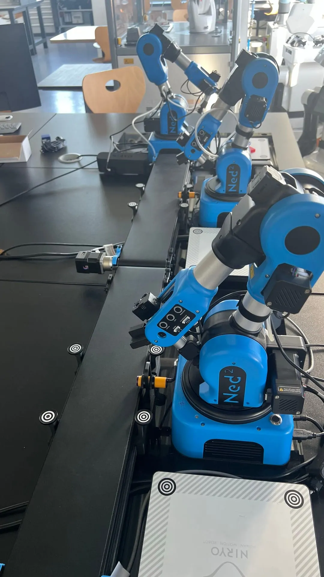 Trois bras robotisés bleus alignés sur un plan de travail, reliés par des convoyeurs.